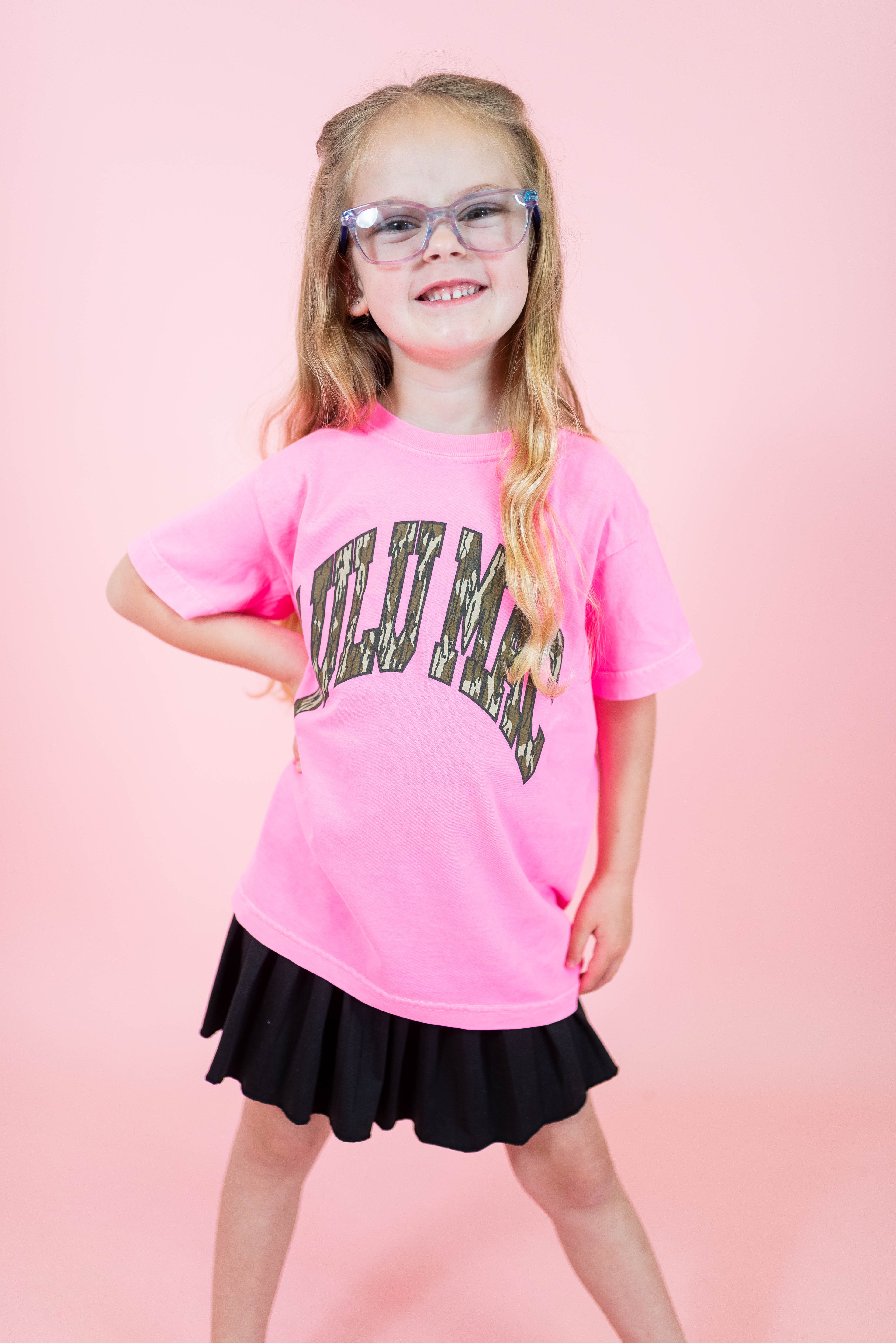 Young girl wearing a pink t-shirt with text and a black skirt on a pink background