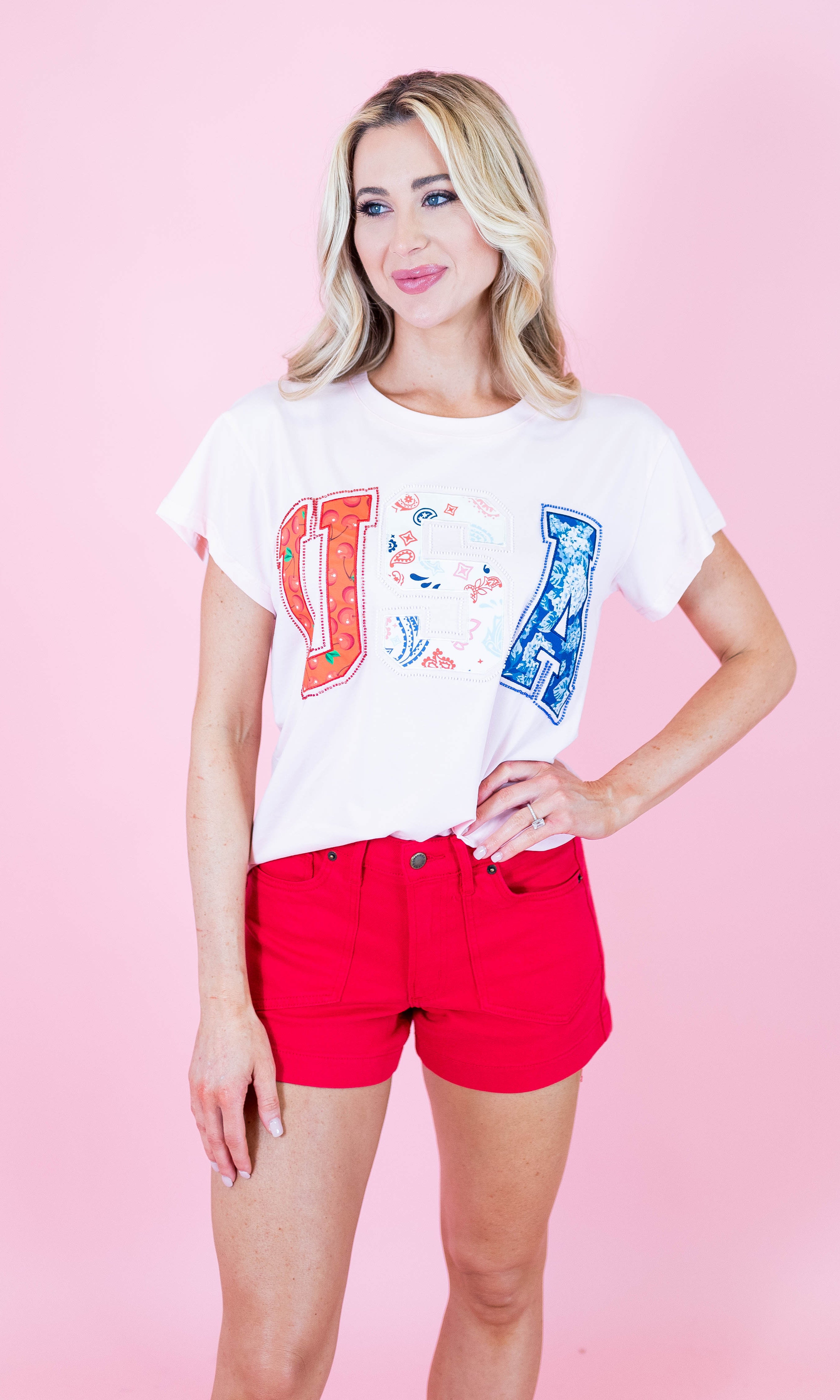 Woman wearing a white t-shirt with colorful graphics and red shorts on a pink background