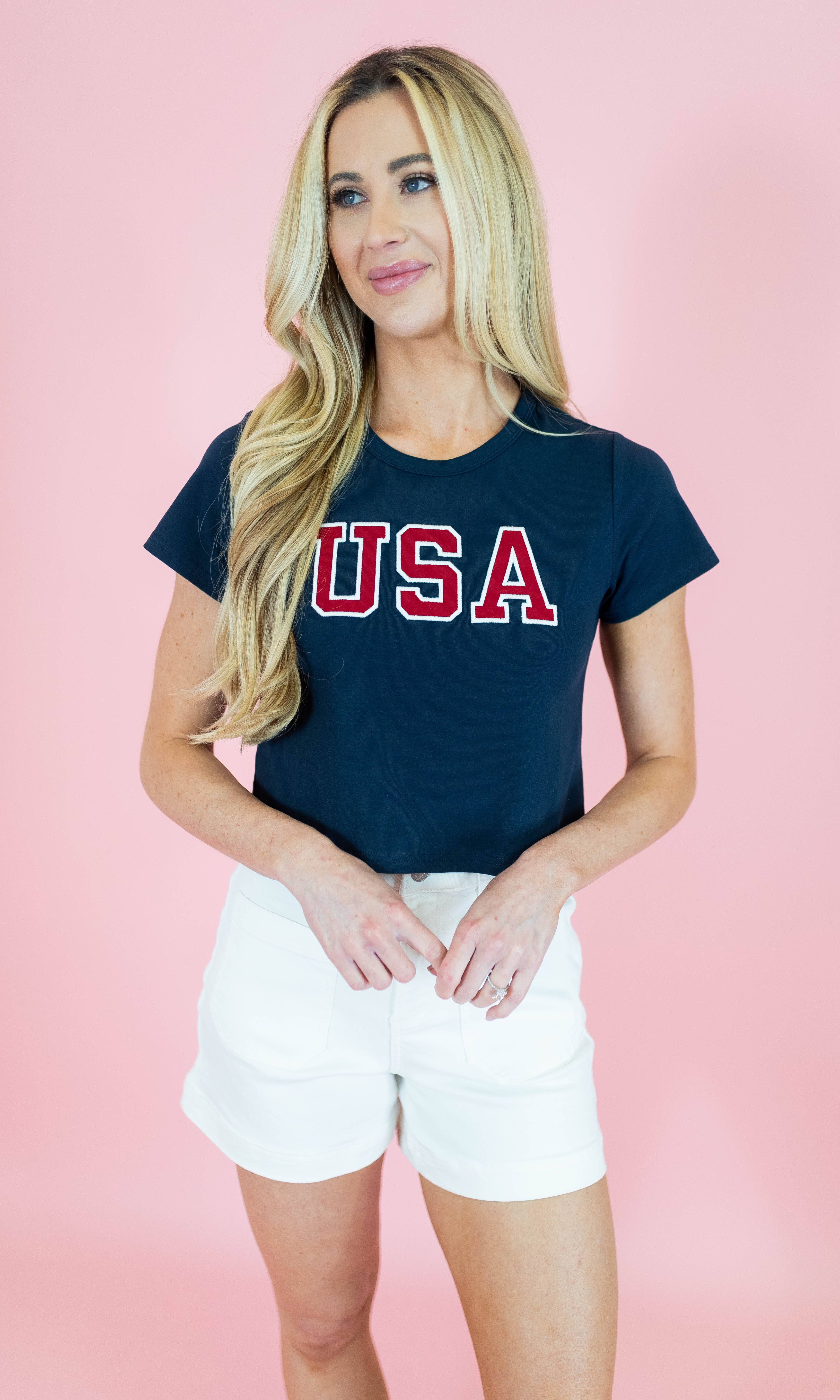 Woman wearing a navy blue t-shirt with 'USA' printed in red on a pink background