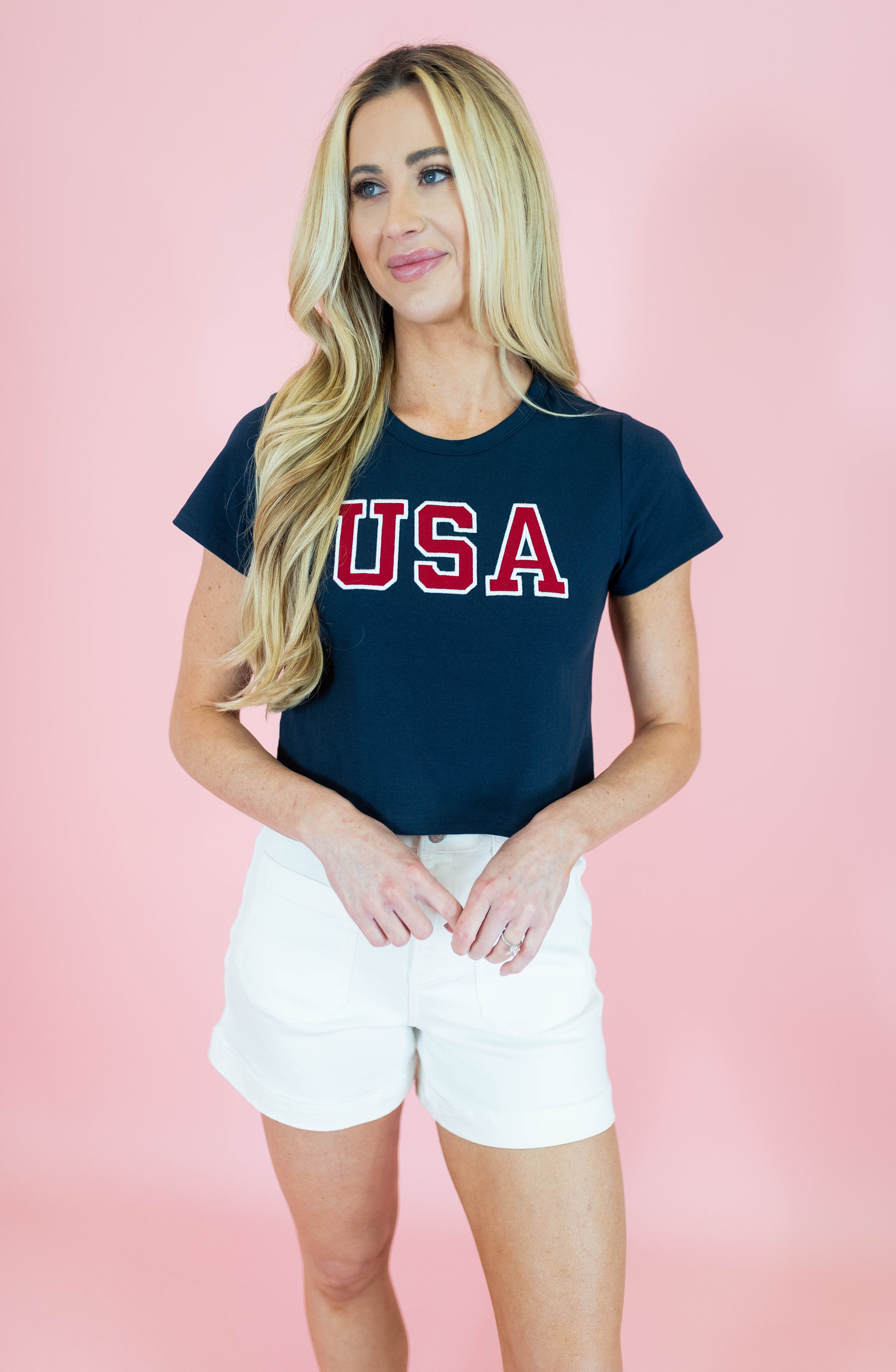 Woman wearing a navy blue t-shirt with 'USA' printed in red on a pink background