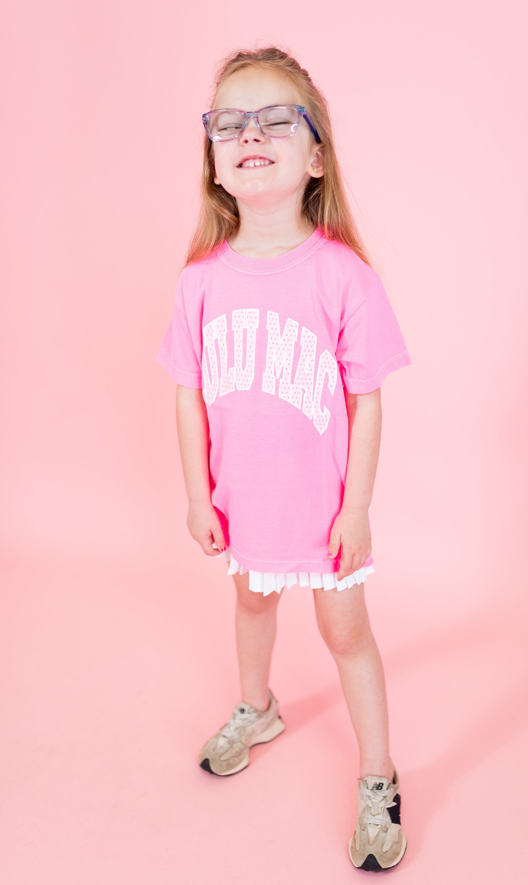 Young girl wearing a pink t-shirt with text and white shorts on a pink background