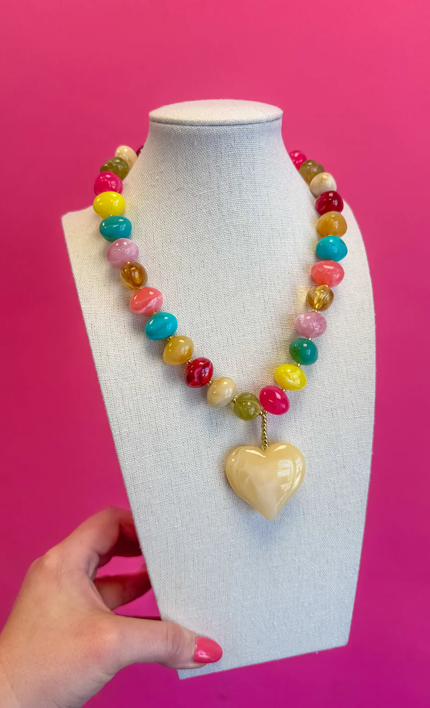 Colorful beaded necklace with a heart-shaped pendant on a mannequin bust against a pink background.