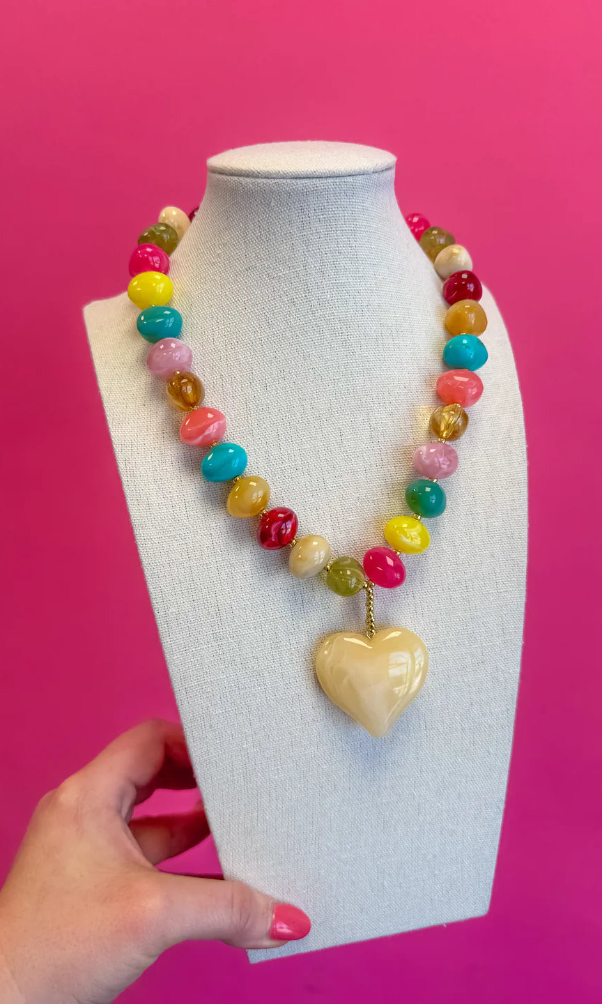 Colorful beaded necklace with a heart-shaped pendant on a mannequin bust against a pink background.