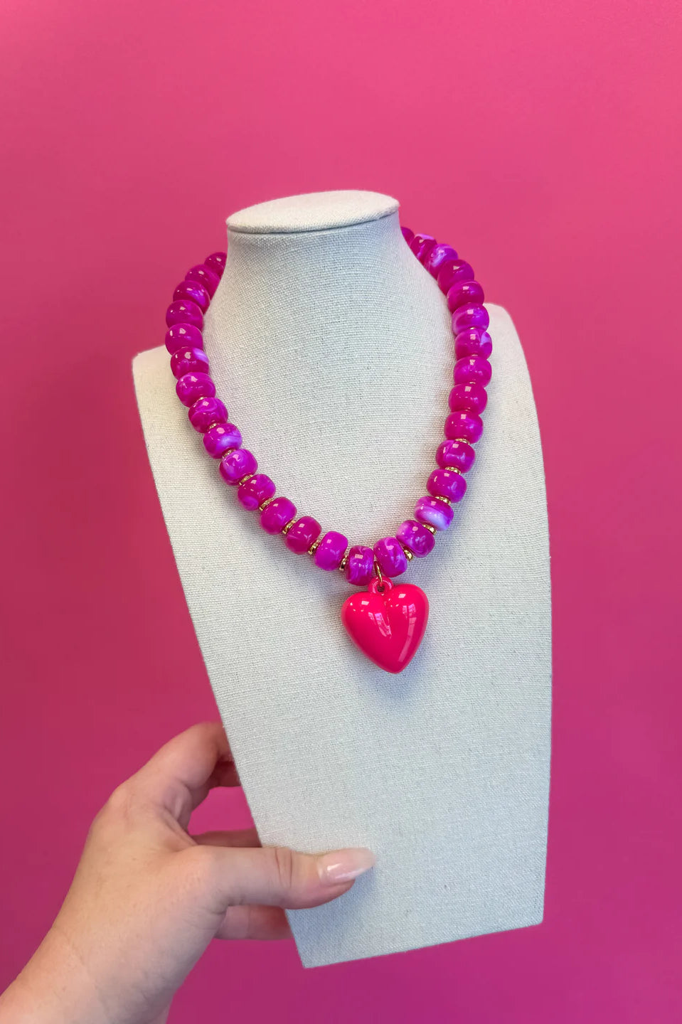 Pink beaded necklace with a heart pendant on a mannequin bust against a pink background