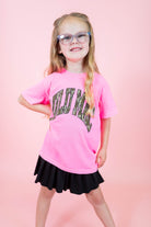 Young girl wearing a pink t-shirt with text and a black skirt on a pink background