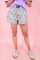 Person wearing patterned shorts with a visible brand label on a pink background