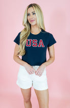 Woman wearing a navy blue t-shirt with 'USA' printed in red on a pink background