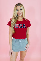 Woman wearing a red 'USA' t-shirt and striped skirt on a pink background