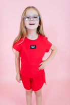 Young girl wearing a red outfit with a visible brand logo on a pink background