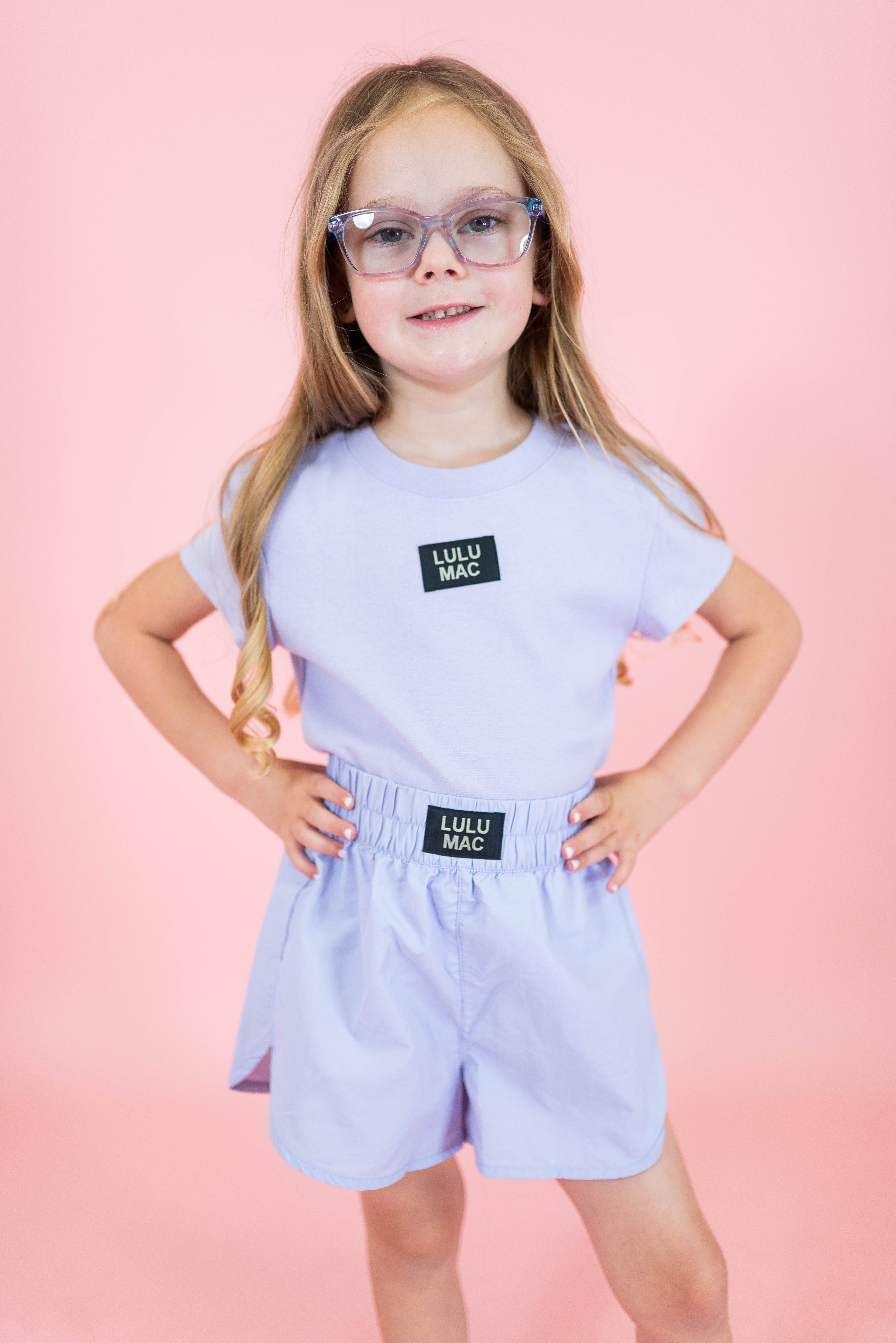 Young girl wearing a light purple outfit with 'Lulu Mac' branding on a pink background
