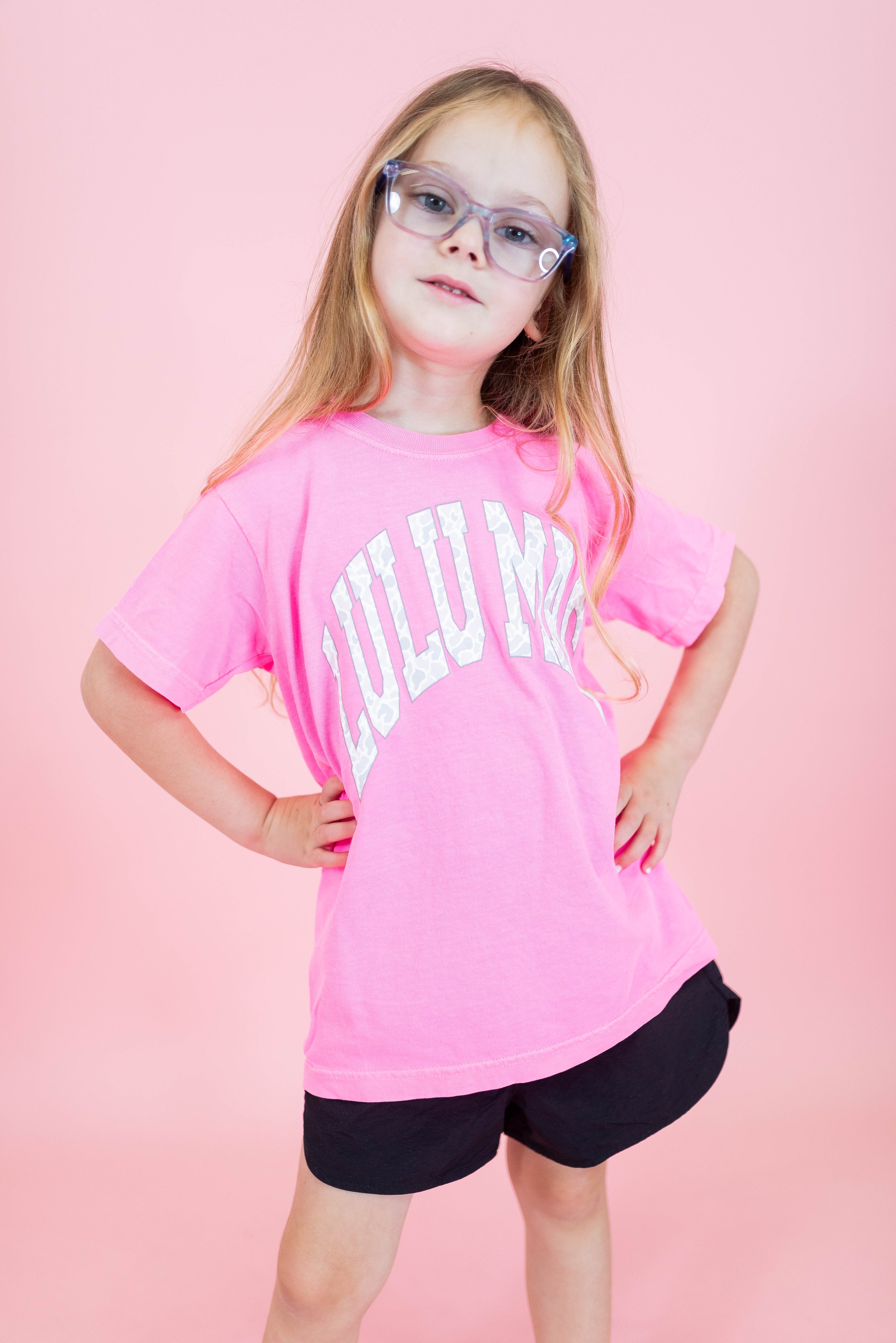 Young girl wearing a pink 'LULUM' t-shirt against a pink background