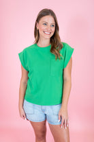 Woman wearing a green top with a pocket on a pink background