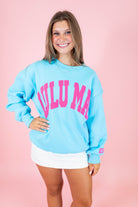 Woman wearing a light blue sweatshirt with pink text on a pink background