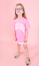 Young girl wearing a pink t-shirt with text and white shorts on a pink background