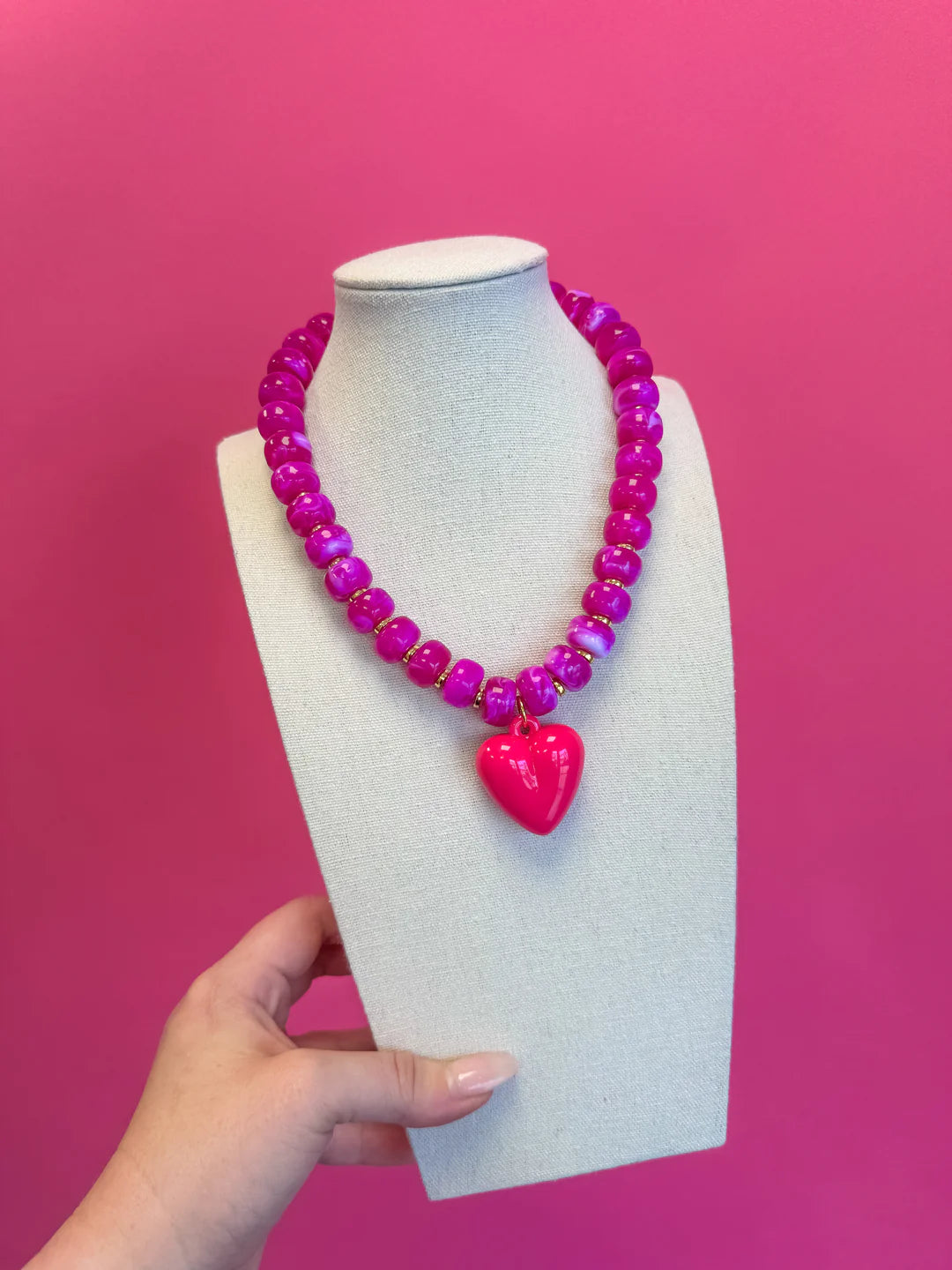 Pink beaded necklace with a heart pendant on a mannequin bust against a pink background
